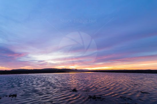 Sun setting behind distant hills over sea