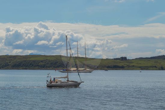 Smaller yacht motors past lager three masted yacht in background. Largs, Scotland