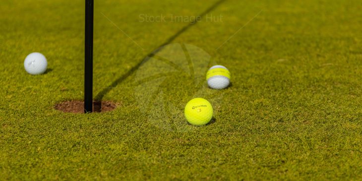 Golf Balls sitting next to pin on golf green image