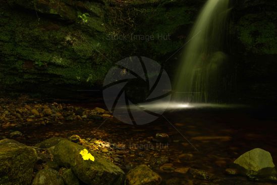 Secluded waterfall deep within woodland as sun just peeps through the canopy of trees overhead