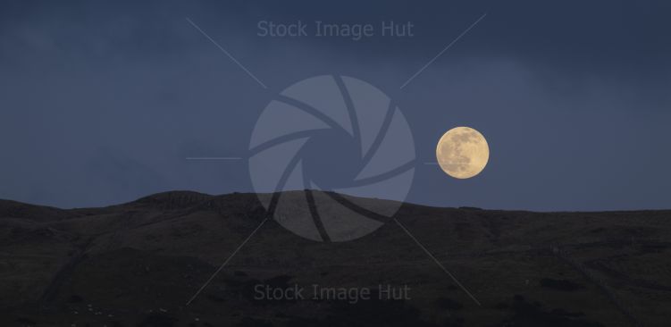 A new full moon just rising over hills as sun lights it up