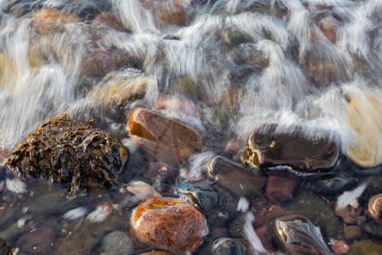 Tide coming in over pebbles on beach making them gleam
