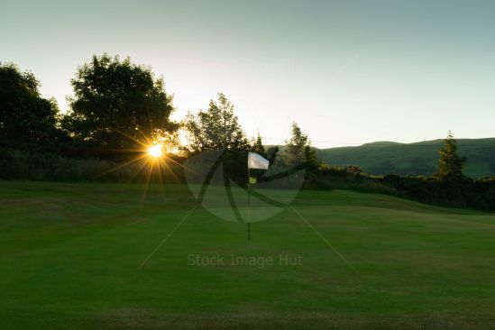 Beautiful starburst peeping through trees as sun begins to rise over golf course