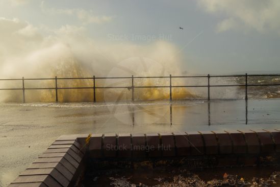Sunshine lights up huge waves as they crash against promenade